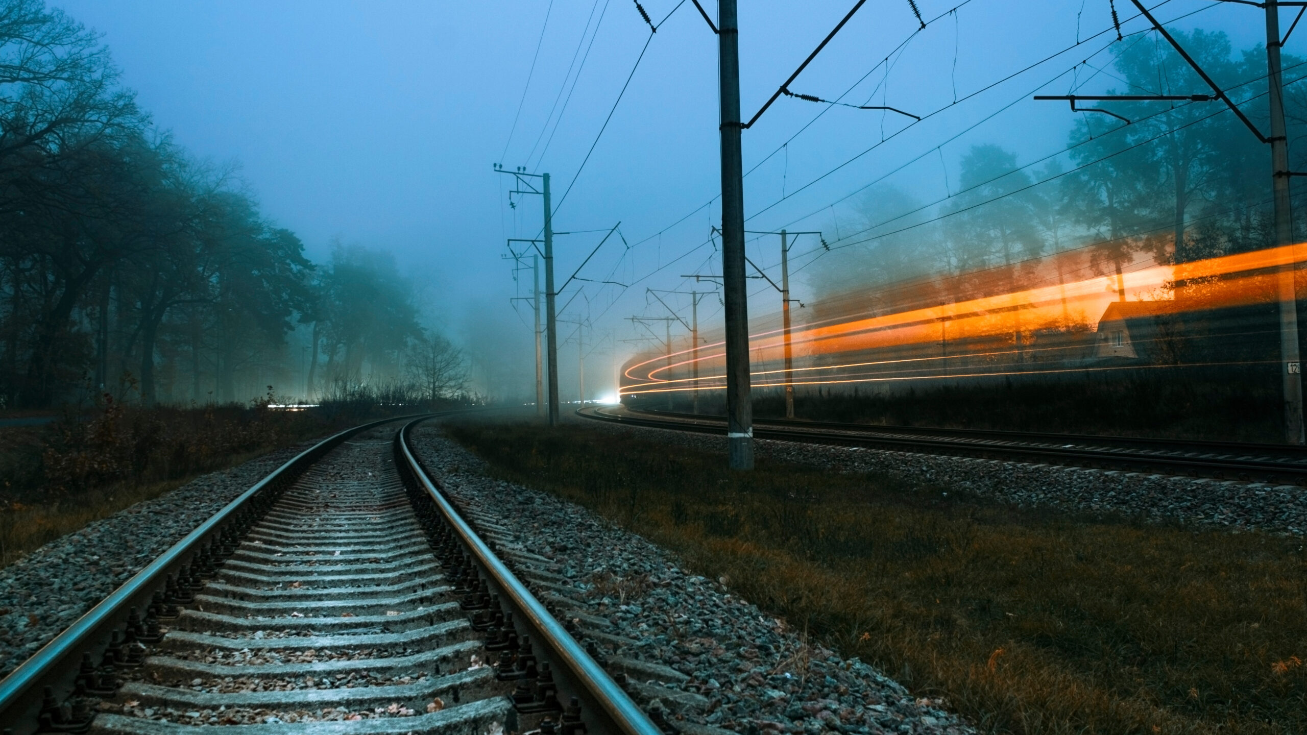 Railroad on a foggy evening. Blurry lights of a passing train. Fast passing train. Gloomy cold evening.