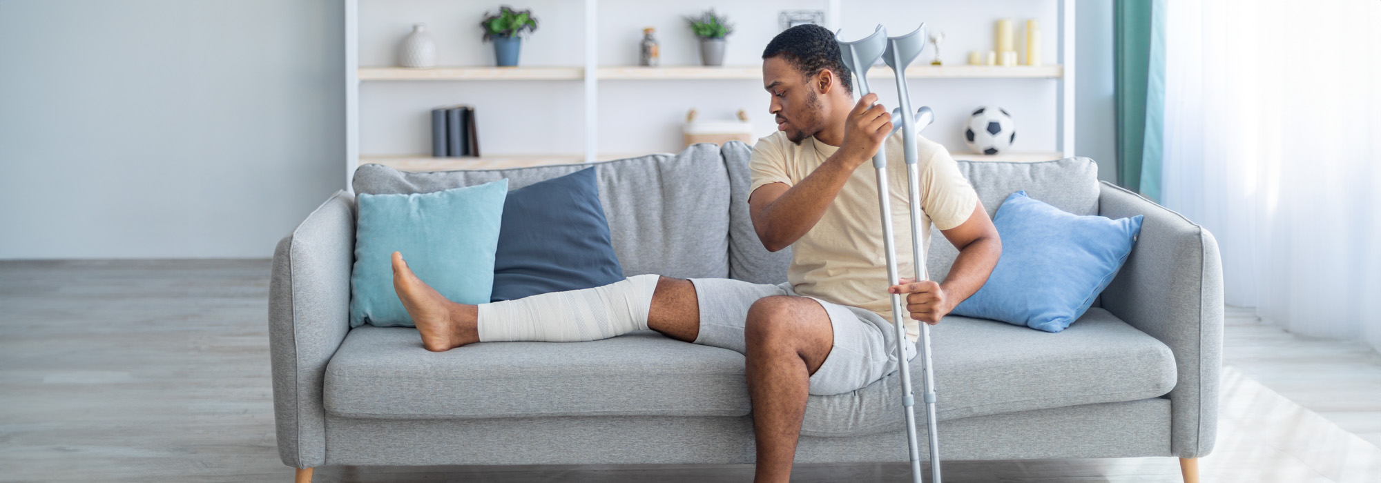 african american guy with plastered leg sitting on sofa